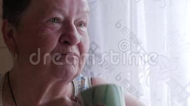 一位老妇人端着一杯热饮和饮料。 他坐在窗边吃早餐。 简单的家居服。